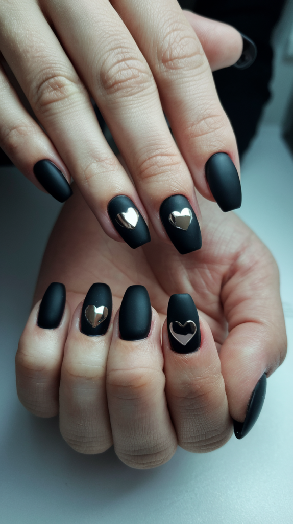 Close up of nails featuring elegant matte black with gold heart designs.
