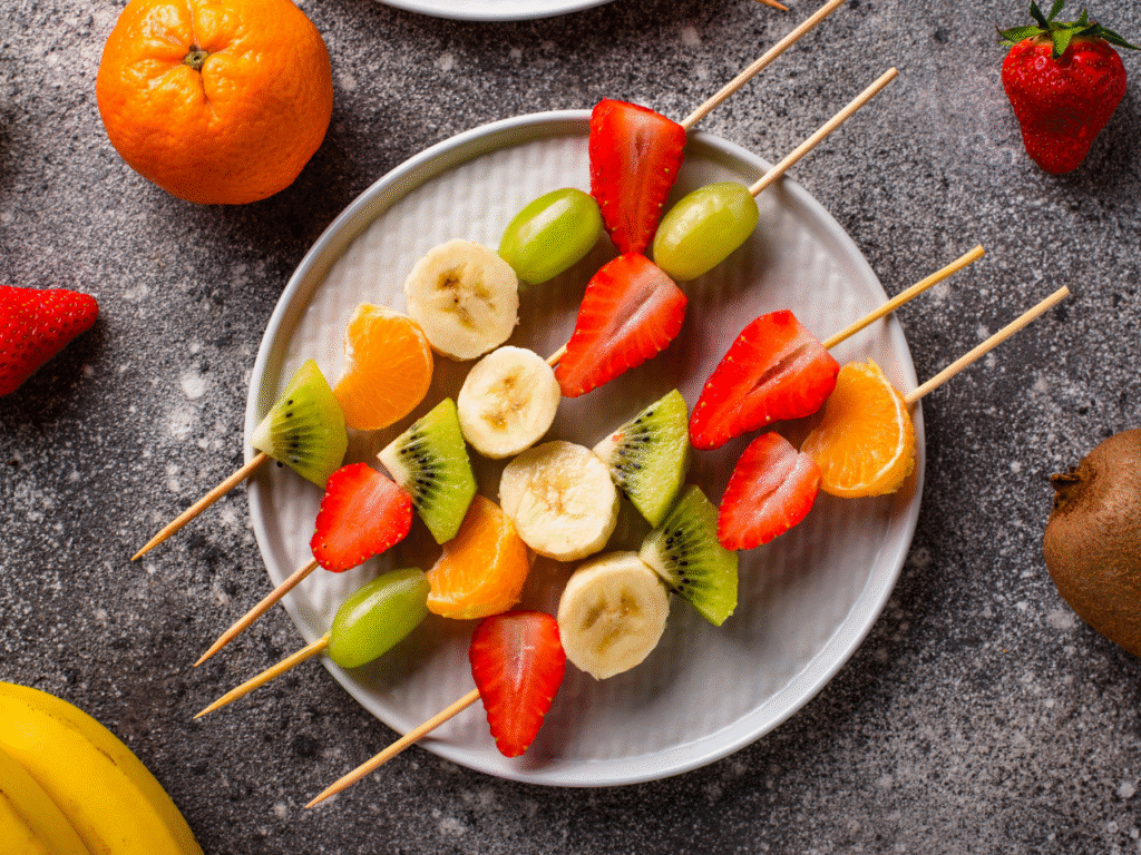 5 A close-up of a bento box featuring colorful fruit skewers with berries, melon, and grapes, next to a small container of yogurt dip. Also, some cheese and veggie skewers with cherry tomatoes, cucumber, and cheese cubes. Bright, natural lighting.