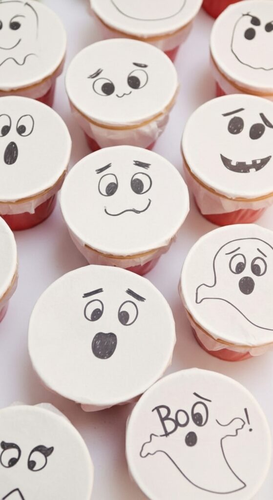 A DIY Poke-a-Ghost Halloween party game for kids, white tissue paper ghosts over cups, cute spooky faces, realistic photo with Halloween decorations.