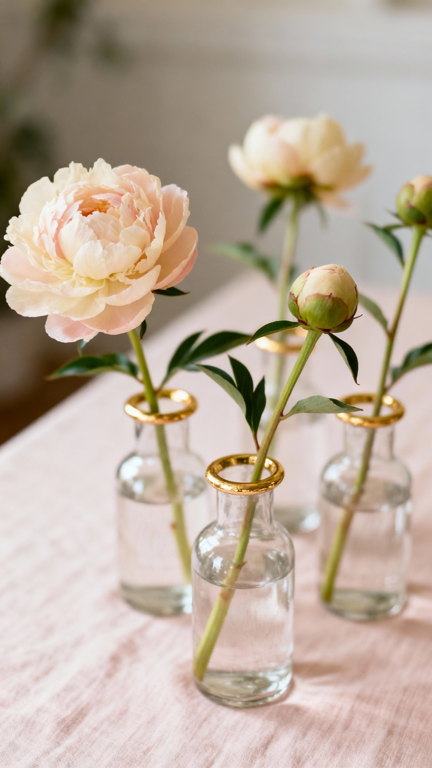 Closeup clustered bud vases with single peonies, blush-ivory linens, gold accents